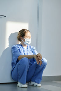 Nurse wearing protective face mask squatting in front of wall at hospital