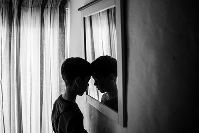 Side view of boy standing by mirror
