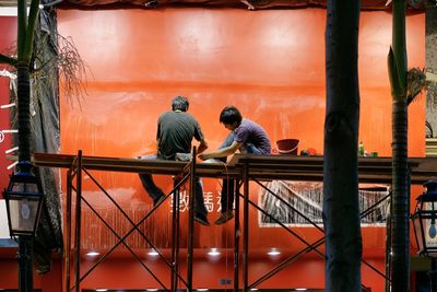 Rear view of men sitting against orange sky