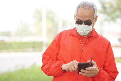 Senior man wearing mask using mobile phone outdoors