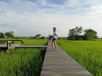 Man cycling on footpath amidst field against sky