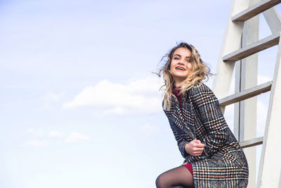 Smiling young woman standing against sky