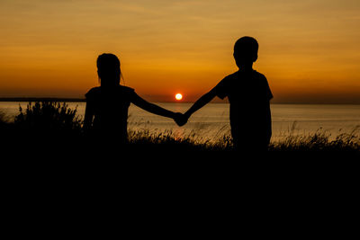 Silhouette people standing on land against sky during sunset