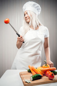 Young woman holding vegetables with knife while standing in kitchen