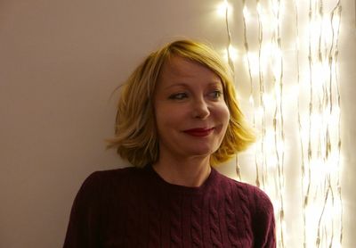 Close-up of woman looking away while standing by illuminated string lights on wall