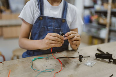 Midsection of student connecting electric plugs on table at school workshop