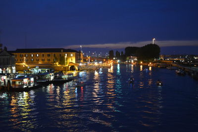 Illuminated buildings by river against sky at night