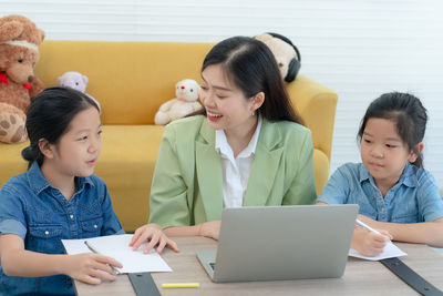 Young asian mother teaching her child to do homework in living room. homeschooling concept