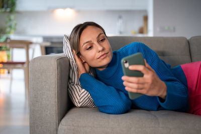Young pensive woman in blue sweater reads bad news message from boyfriend in social media on phone