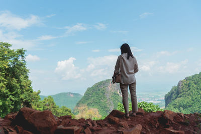 Rear view of woman standing on rock against sky