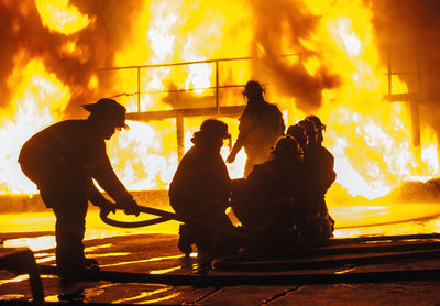 Silhouette firefighters spraying water on fire at night