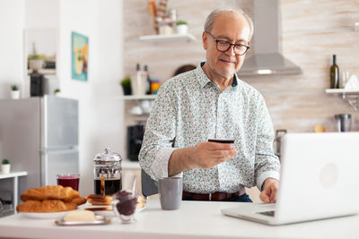 Senior man holding credit card while using laptop at home