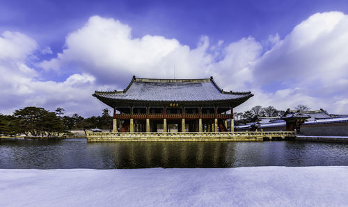 View of building by lake against cloudy sky