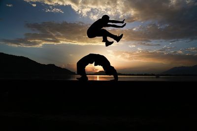 Silhouette people jumping on beach at sunset