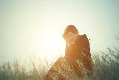 Sad woman sitting on field against sky during sunset