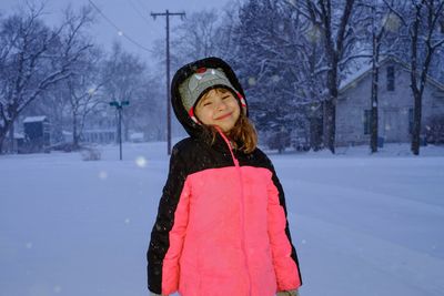 Portrait of smiling girl standing on field during snowfall