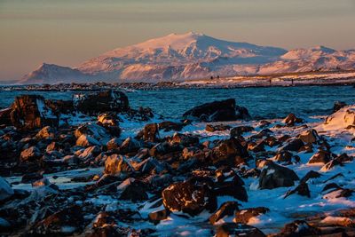 Scenic view of sea by mountain against sky during winter