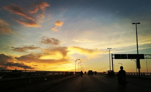 Silhouette man on road against sky during sunset