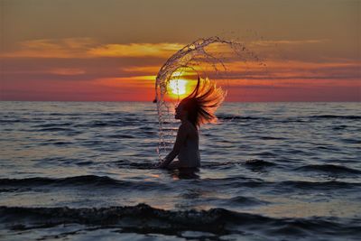 Woman standing at sea against sky during sunset