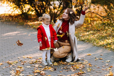 Happy mom and child are walking and having fun playing with autumn leaves in the fall park outdoors