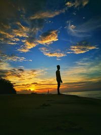 Silhouette man standing on beach against sky during sunset