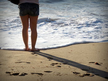 Low section of woman standing on shore at beach