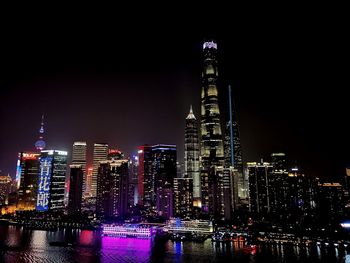 Illuminated modern buildings in city against sky at night