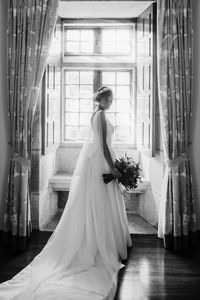 Full length of bride holding bouquet standing at home