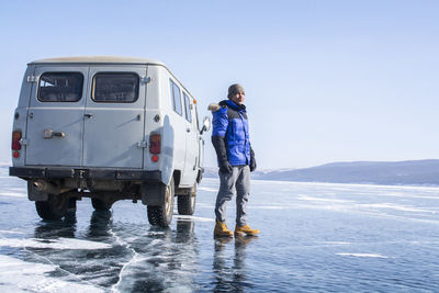 Man standing by van on frozen lake against sky