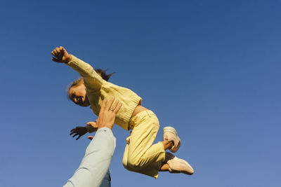 Hands of carefree man holding aloft daughter under blue sky