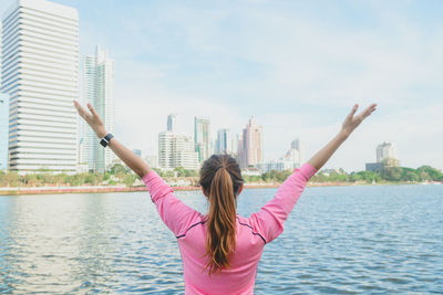 Rear view of woman with arms outstretched against cityscape