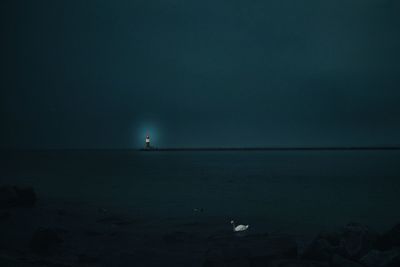 Lighthouse by sea against sky at night