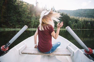 Full length of young woman sitting on boat against lake