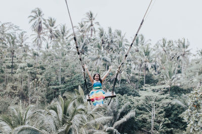 Rear view of woman hanging amidst trees against sky