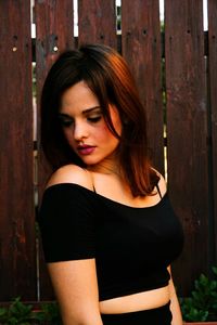 Young woman standing by wooden fence