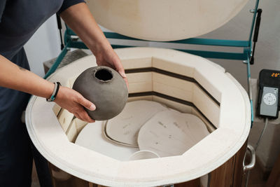 Close-up of hands putting vase into the kiln, oven for roasting of unbaked clay handmade products