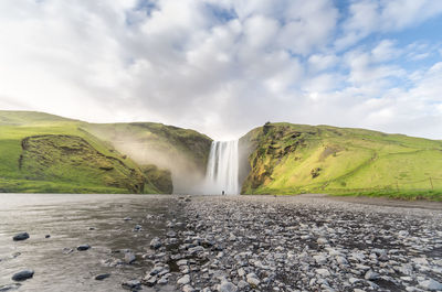 Scenic view of skogafoss waterfall on mountain against sky