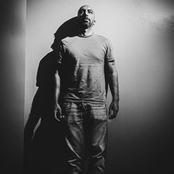 Young man looking away while standing against wall
