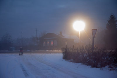 Snow covered road by buildings against sky during winter