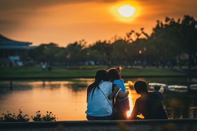 Rear view of people sitting on shore against sky during sunset