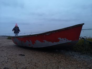 Girl standing on boat moored at beach against sky