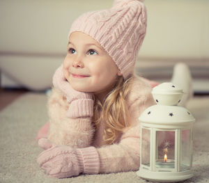 Close-up of cute girl wearing warm clothing holding oil lamp at home