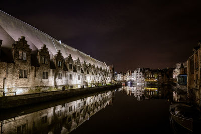 Illuminated buildings by canal against sky at night