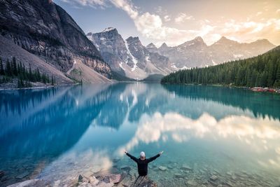 Man with arms raised standing by lake against mountains