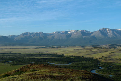 River in a high-mountain valley with hills and a ridge at dawn in summer, forest around the river