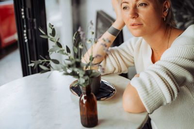 Woman sitting at table in cafe looking at window with dreamy look