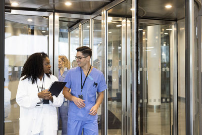 Male and female doctor talking while walking through revolving door