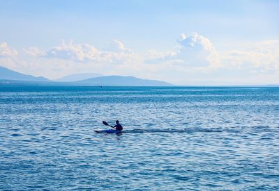 Man rowing kanoe in sea against sky