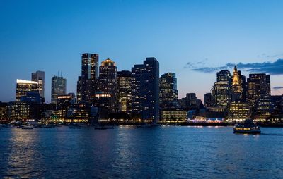 Illuminated city at waterfront against blue sky