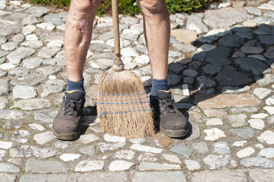 Gardener in dirty work clothes and boots holds garden tools, tools brush broom